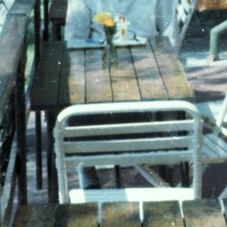 Two elderly people sitting and standing outdoors on a rainy day.