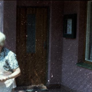 Two elderly people sitting and standing outdoors on a rainy day.