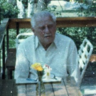 Two elderly people sitting and standing outdoors on a rainy day.