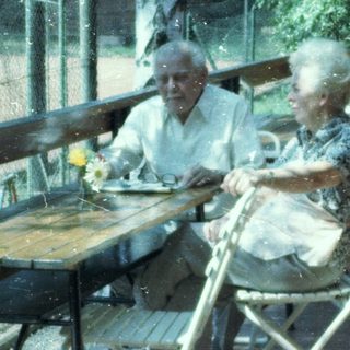 Two elderly people sitting outdoors at a café table.