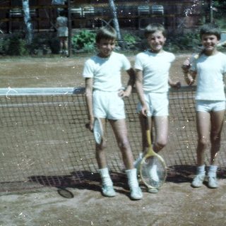 Four children holding tennis rackets on outdoor court.
