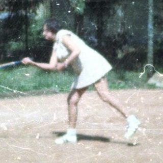 Person playing tennis on outdoor clay court.