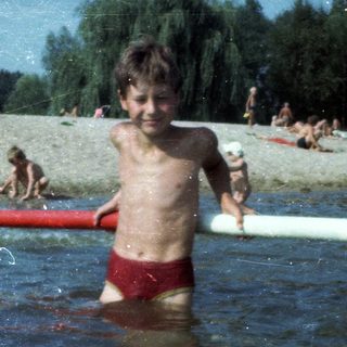 Shirtless boy playing in shallow water at beach.
