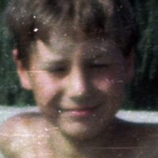Shirtless boy playing in shallow water at beach.