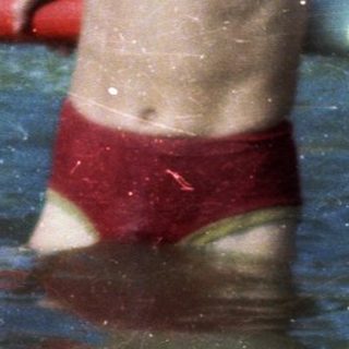 Shirtless boy playing in shallow water at beach.