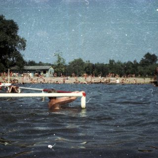 Busy lake scene with people swimming and boating.