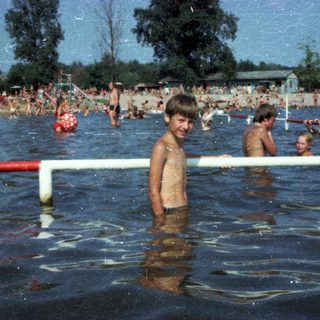 Boy standing in crowded outdoor swimming pool.