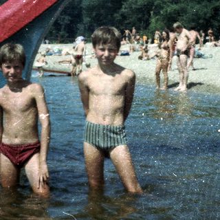 Two boys playing in shallow water at a crowded beach.