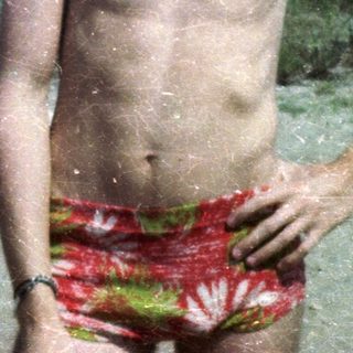 Two shirtless young men posing outdoors by water.