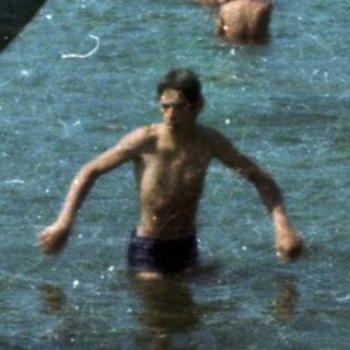 People swimming and playing in a lake with a red slide.