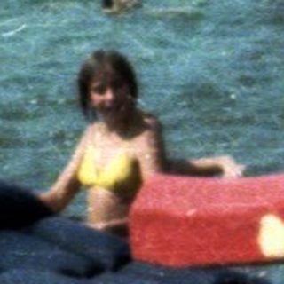 People swimming and playing in a lake with a red slide.