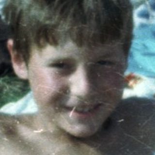 Boy sitting wet on grass blanket at outdoor picnic.
