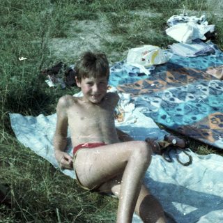 Boy sitting wet on grass blanket at outdoor picnic.
