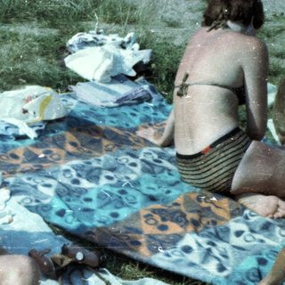 Boy sitting wet on grass blanket at outdoor picnic.