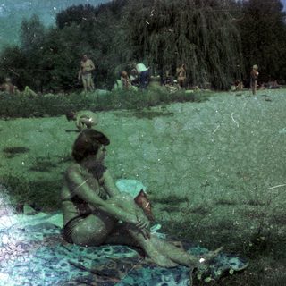 People relaxing outdoors by water in grassy park area.
