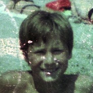 Boy playing joyfully in green, muddy water.