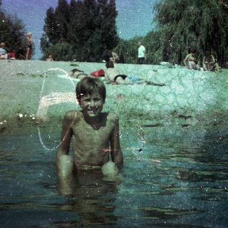 Boy playing joyfully in green, muddy water.