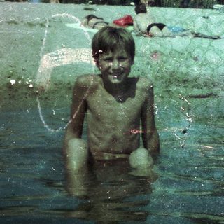 Boy playing joyfully in green, muddy water.