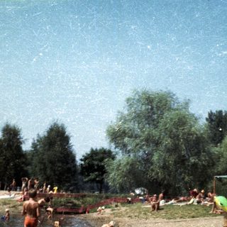 People swimming and sunbathing by a lake.