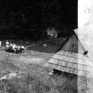 Group of people fishing by a stream near rustic cabins.