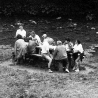 Group of people fishing by a stream near rustic cabins.