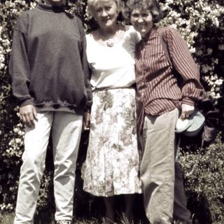 Three people posing together in a garden with blooming trees.