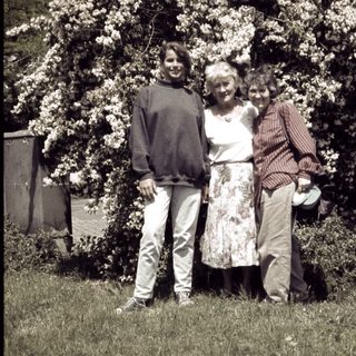 Three people posing together in a garden with blooming trees.