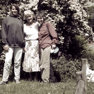Three people posing together in a garden with blooming trees.