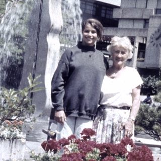 Two people posing beside modern fountain sculpture and blooming flowers.