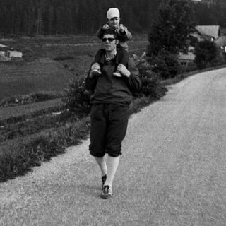 Person carrying child on back walks along rural road.