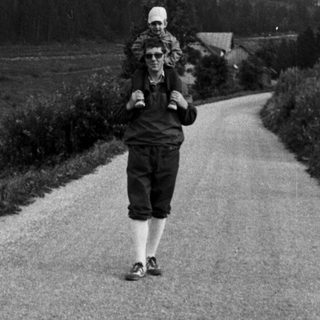 A person carrying a child walks on a rural road.