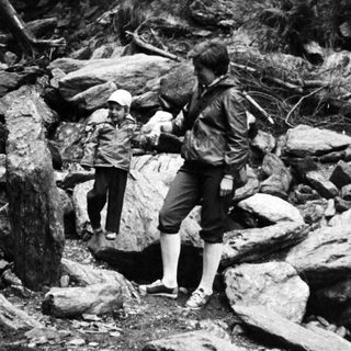 Two people hiking through rocky forest terrain.
