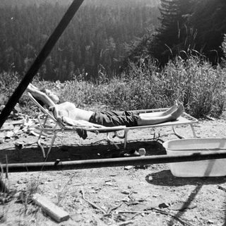 Person relaxing in a deck chair outdoors near forest.