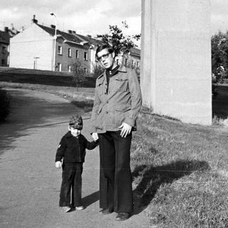 A man and child walking outdoors beside a tall wall.