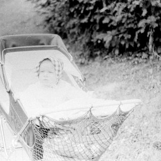 Baby reclining in vintage pram on grass.