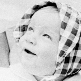 Baby in vintage pram with blanket, outdoors.