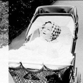 Baby in vintage pram with blanket, outdoors.