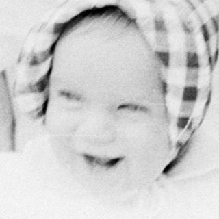 Baby wrapped in blanket smiling in vintage stroller.