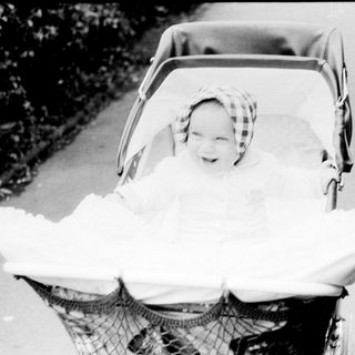 Baby wrapped in blanket smiling in vintage stroller.