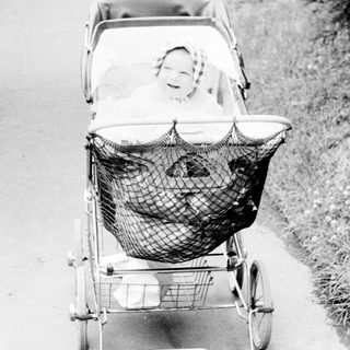 Baby in vintage pram on paved path.