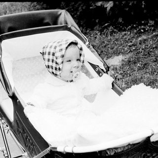 Baby in vintage pram with checkered hat.