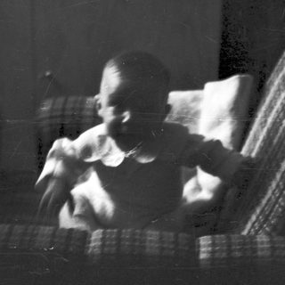 Blurred indoor scene of person sitting on plaid couch.