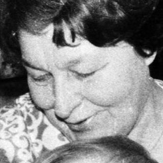 Woman holding baby with stuffed dog indoors.