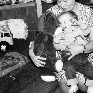 Woman holding baby with stuffed dog indoors.
