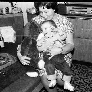 Woman holding baby with stuffed dog indoors.