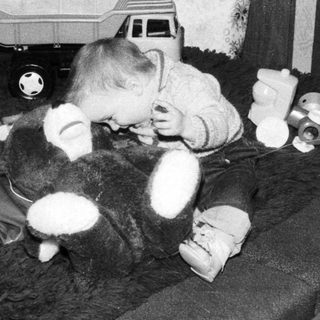 Baby playing with stuffed toys on bed.