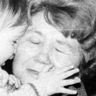 A woman tenderly hugging a baby indoors.
