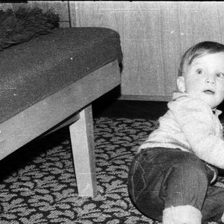 Young child playing with wooden shoe on patterned carpet.