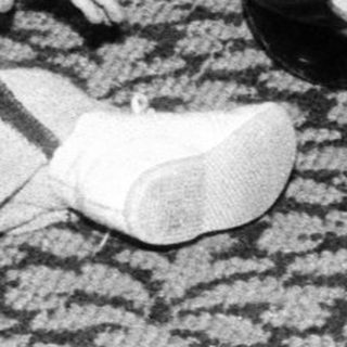 Young child playing with wooden shoe on patterned carpet.