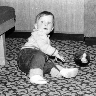 Young child playing with wooden shoe on patterned carpet.
